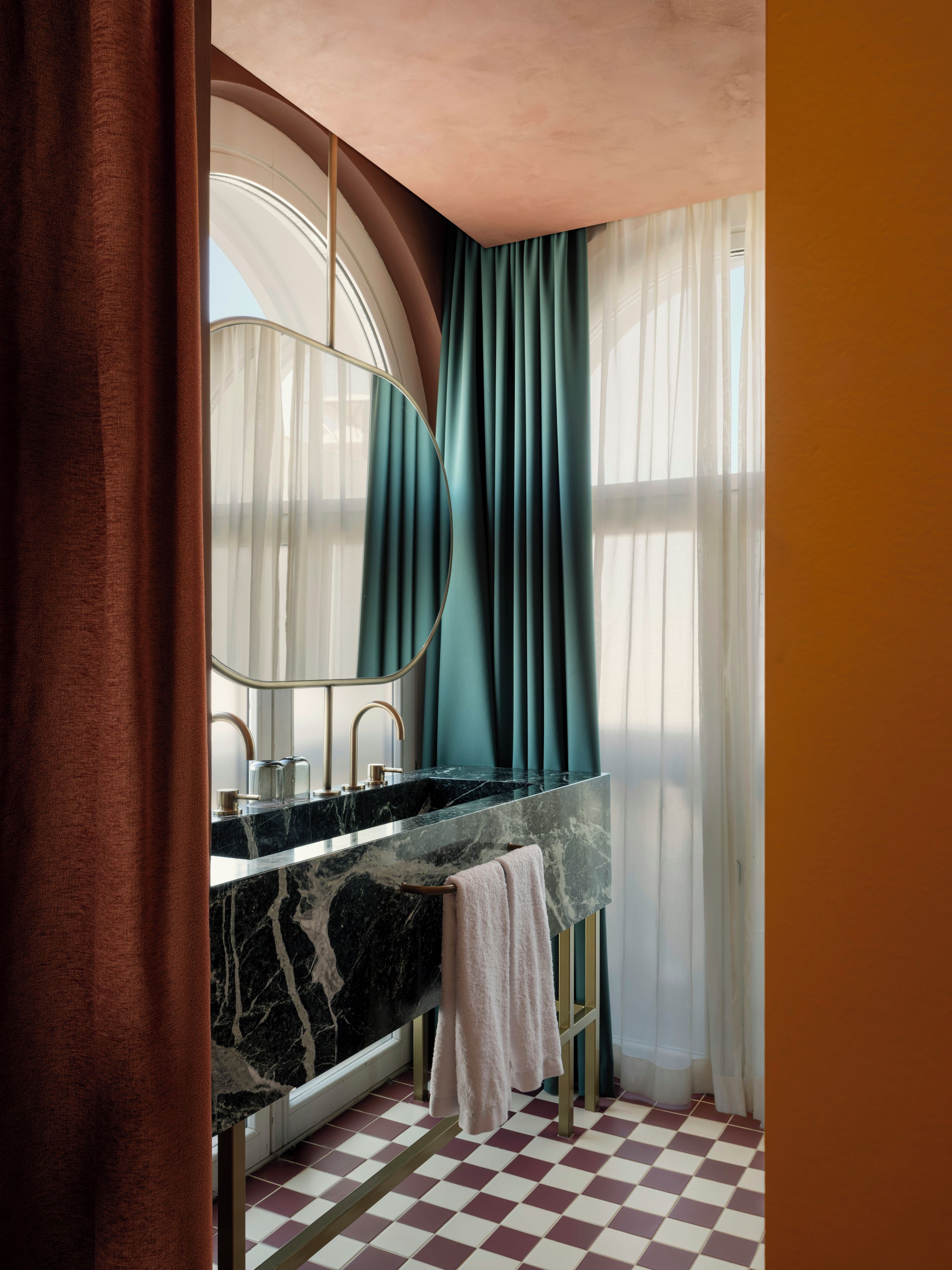 Un baño con lavamanos de mármol, un espejo grande y cortinas color aguamarina.