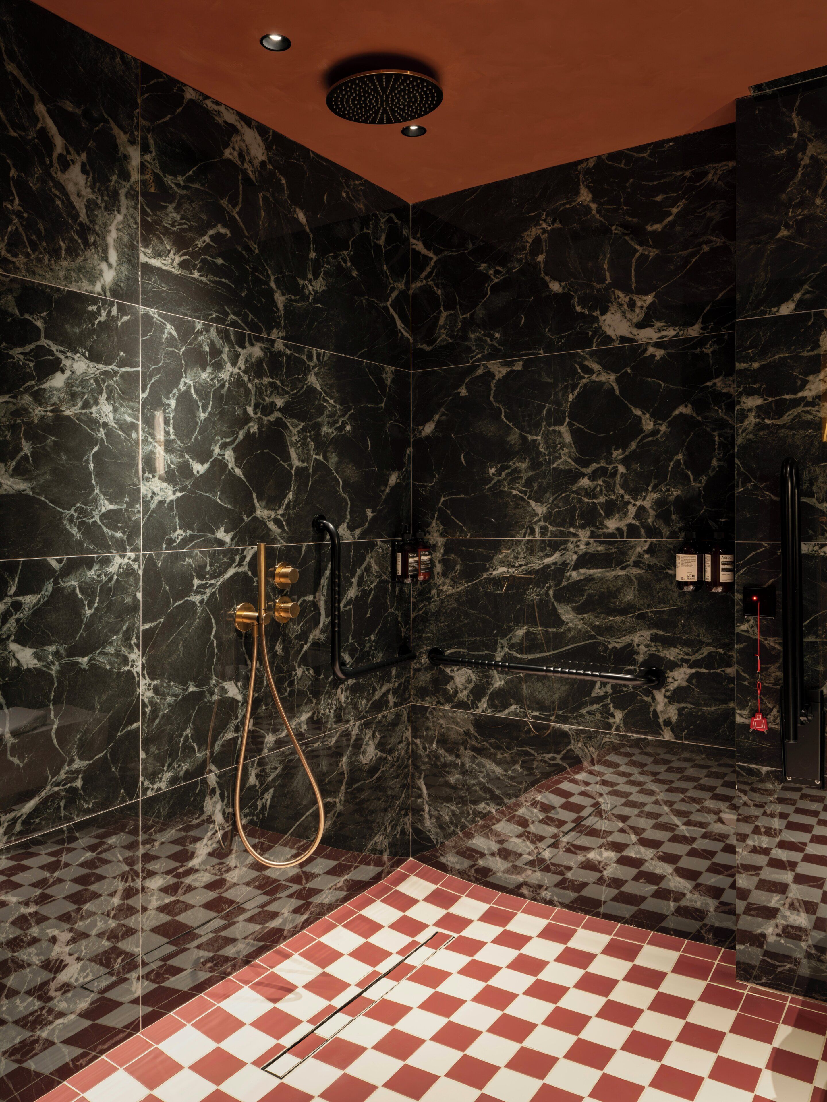 A bathroom with black marble walls, a checkered floor, and a shower with a gold faucet.