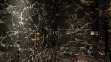 A bathroom with black marble walls, a checkered floor, and a shower with a gold faucet.