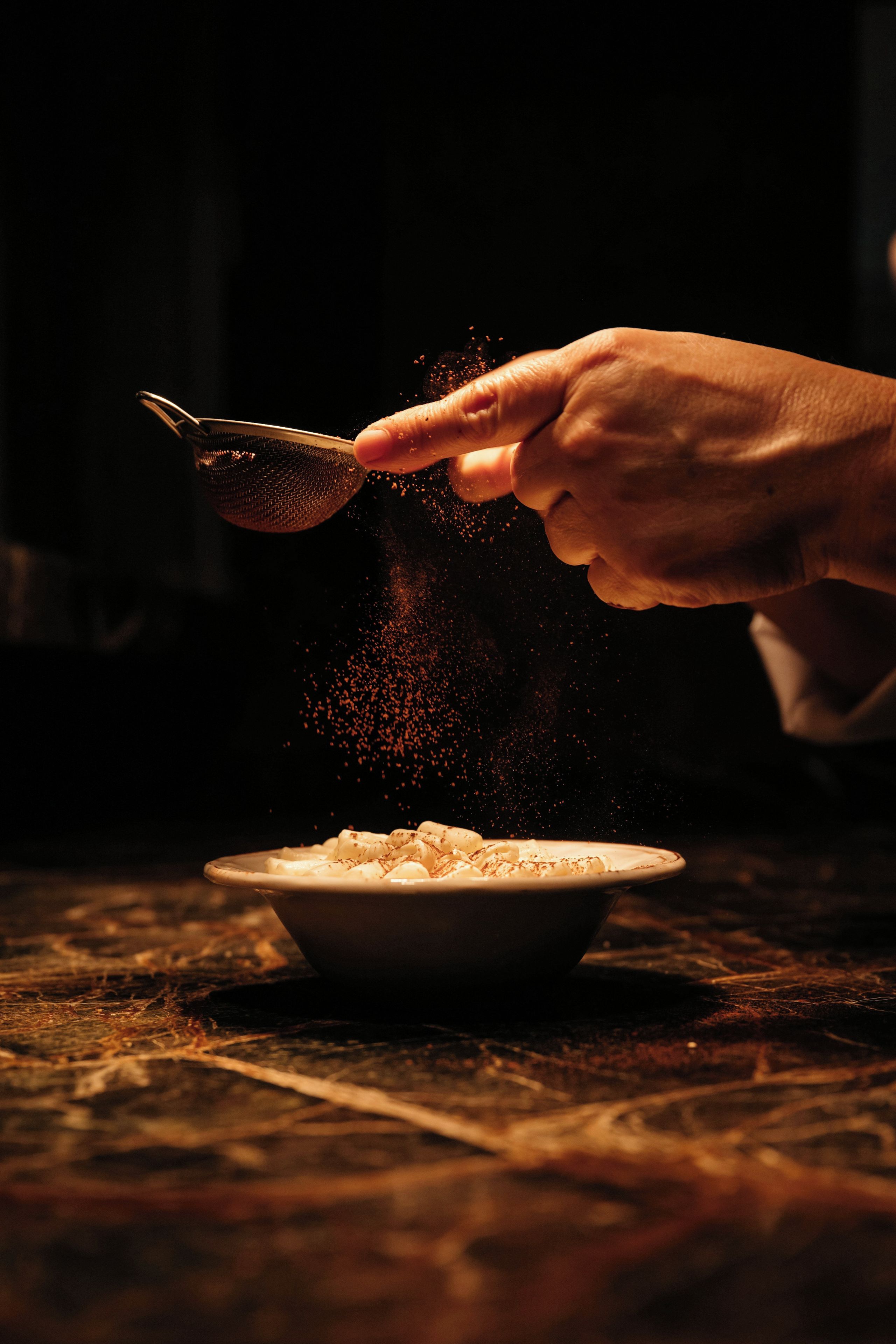 A hand sprinkling a granular substance into a bowl.