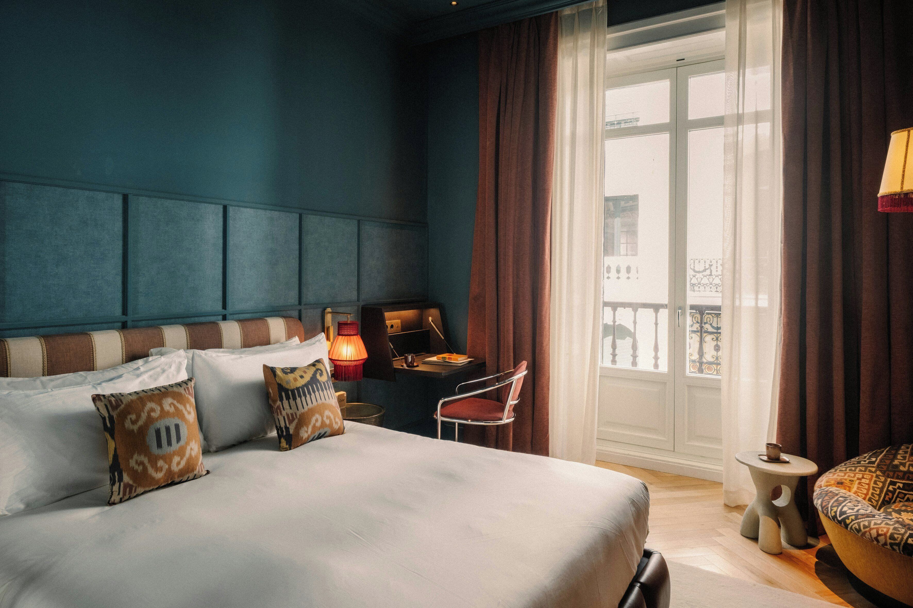A hotel room with a large bed, a desk, a chair, and a view of the outside.