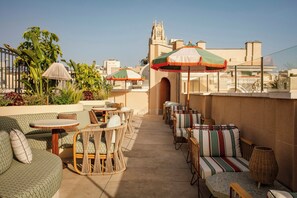 A rooftop terrace with outdoor seating, umbrellas, and a view of a historic building. - Nômade Temple Madrid (Madrid)