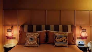 Habitación de hotel con una cama grande, dos lámparas de noche, una mesita con una computadora portátil y un cabecero estampado.