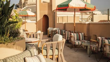 A rooftop terrace with wicker furniture, outdoor umbrellas, and a view of a historic building.