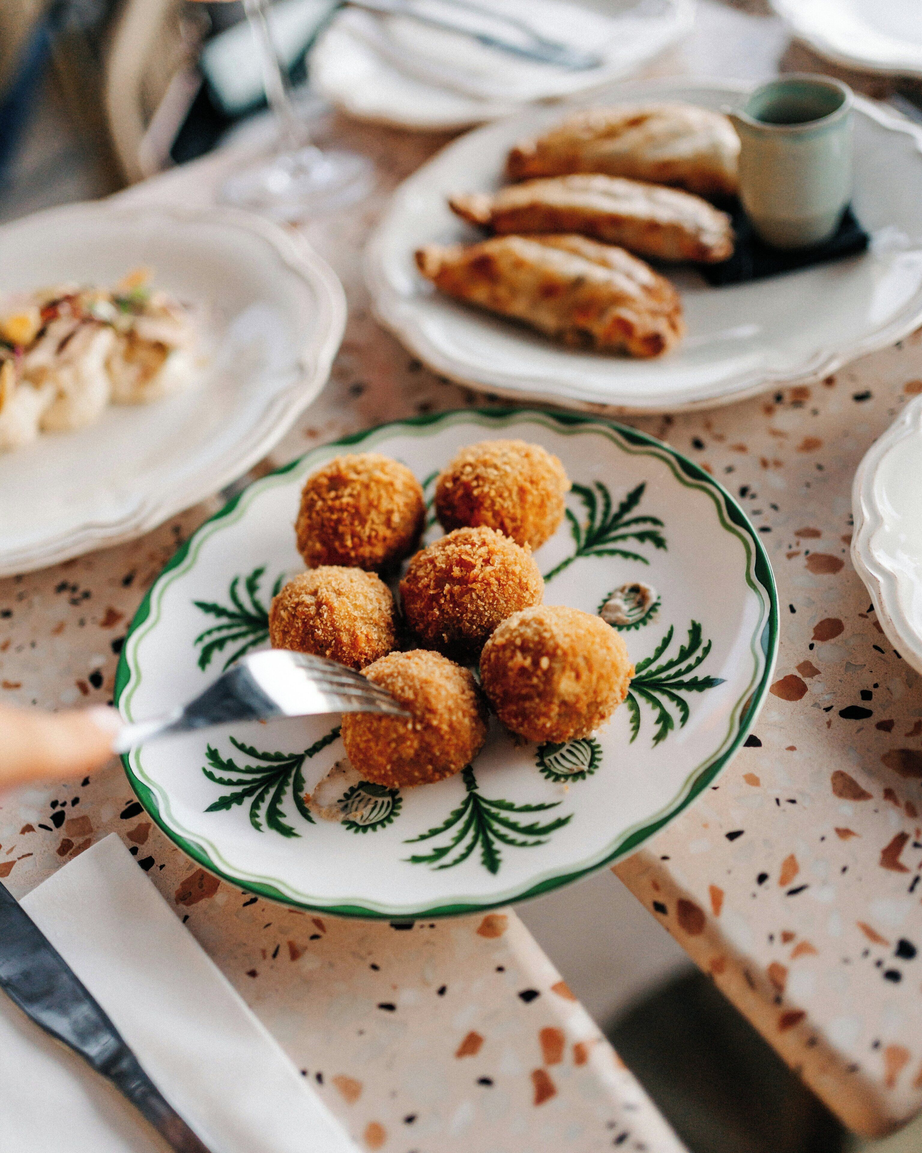 A table with a plate of round, breaded food items, a fork, and a cup.