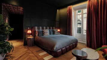 Un dormitorio moderno con una cama grande, lámparas de noche, una mesita redonda y vistas al exterior a través de una ventana.