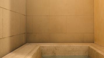Una bañera pequeña y cuadrada con una base rectangular, rodeada de paredes lisas.