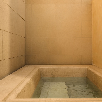 A small, square-shaped bathtub with a rectangular base, surrounded by plain walls.
