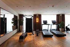 A spacious room with a wooden floor, a treadmill, a stationary bike, a rowing machine, and a bench.
