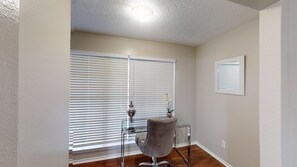 A room with a large window, a chair, and a small table with a vase and an orchid.