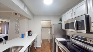 A modern kitchen with stainless steel appliances, a white countertop, and a wooden floor. - I241 - Apt|Patio|10mi to Convention Ctr|Sleeps 4 (Irving)