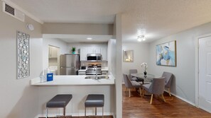 Una cocina moderna con electrodomésticos de acero inoxidable, una isla central con taburetes y un comedor con una mesa redonda y sillas.