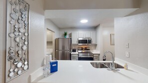 A kitchen with a stainless steel refrigerator, microwave, oven, and sink. There is a blue bag and two water bottles on the counter.