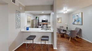 A modern kitchen with stainless steel appliances, a white countertop, and a dining area with a round table and four chairs. - I241 – World Cup Stay - 18 min to AT&T - Sleeps 4 - Public Transit (Irving)
