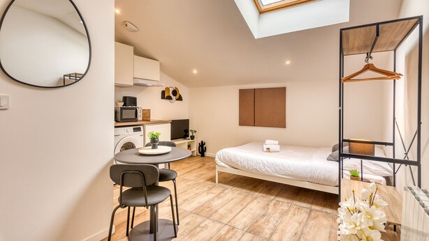 A compact bedroom with a bed, a small table with chairs, a hanging wooden hanger, and a skylight above. - Le Factory - Studio contemporain - Proche métro B (Oullins-Pierre-Bénite)