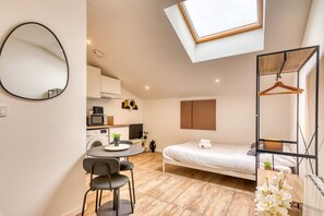 A compact bedroom with a bed, a small table with chairs, a hanging wooden hanger, and a skylight above. - Le Factory - Studio contemporain - Proche métro B (Oullins-Pierre-Bénite)