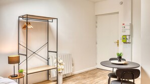 A modern room with a bed, a small table with a plant, a hanging light, and a radiator. - Le Factory - Studio contemporain - Proche métro B (Oullins-Pierre-Bénite)