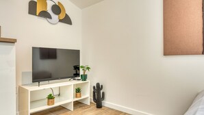 A modern living room with a flat-screen TV on a white stand, a cactus, and two small potted plants. - Le Factory - Studio contemporain - Proche métro B (Oullins-Pierre-Bénite)