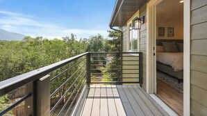 A balcony with a wooden floor and metal railing, overlooking a lush green landscape and a mountain in the distance. - New Ski/Summer Home (Cottonwood Heights)