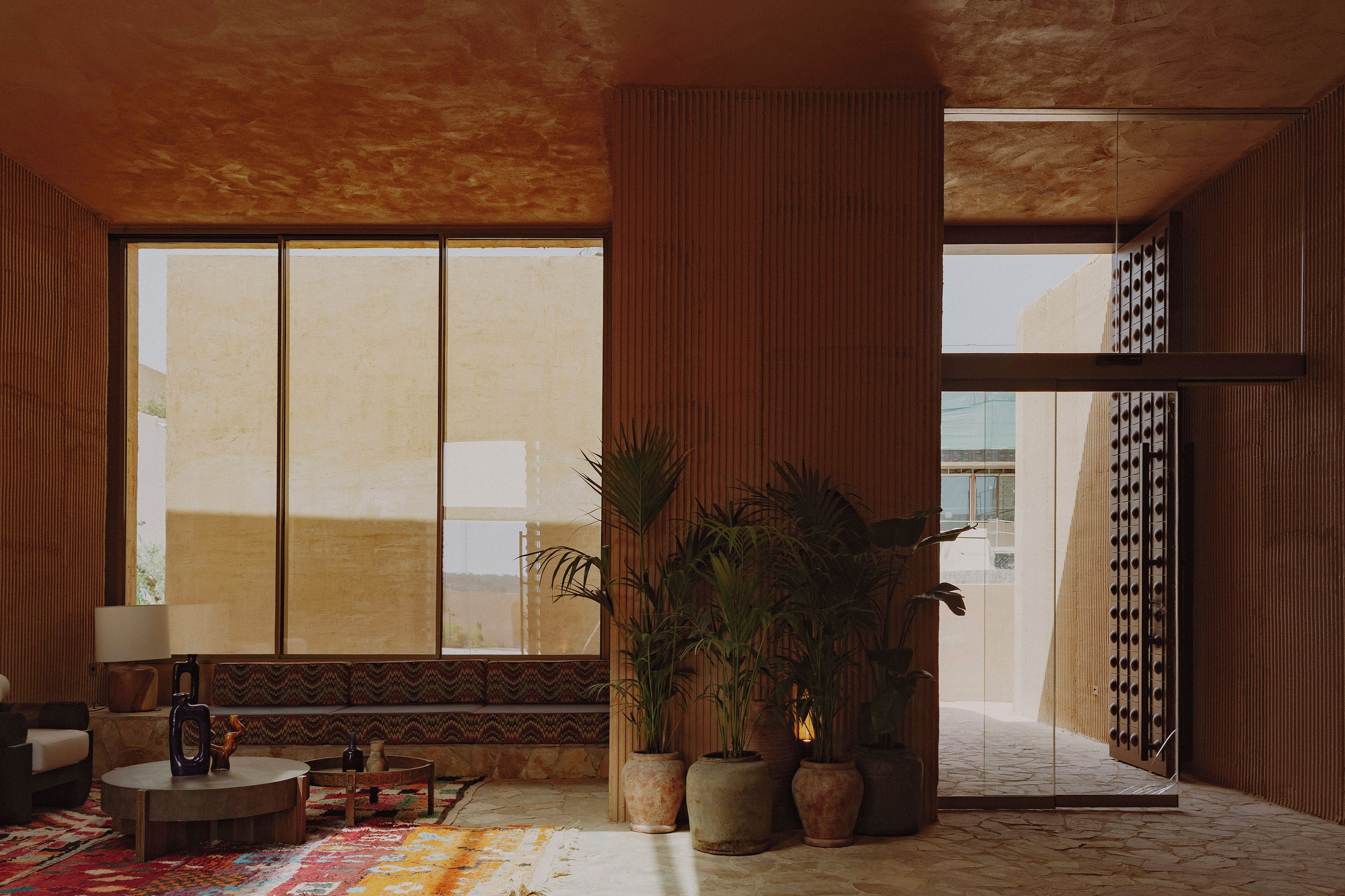 A room with a large window, a wooden floor, a sofa, a coffee table, and several potted plants.