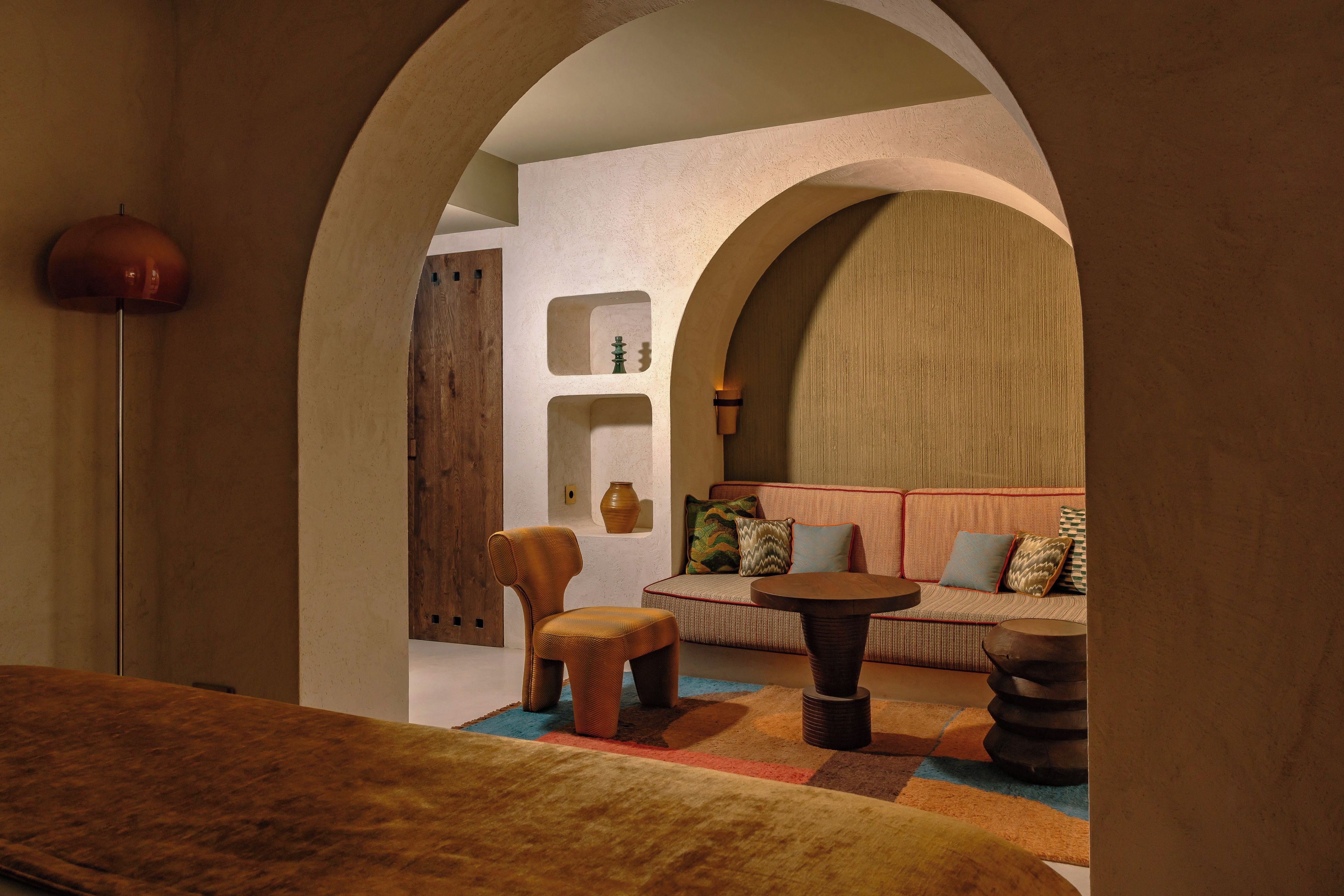 A cozy interior with a sofa, a small table, and a chair. There is a wooden door and a lamp.