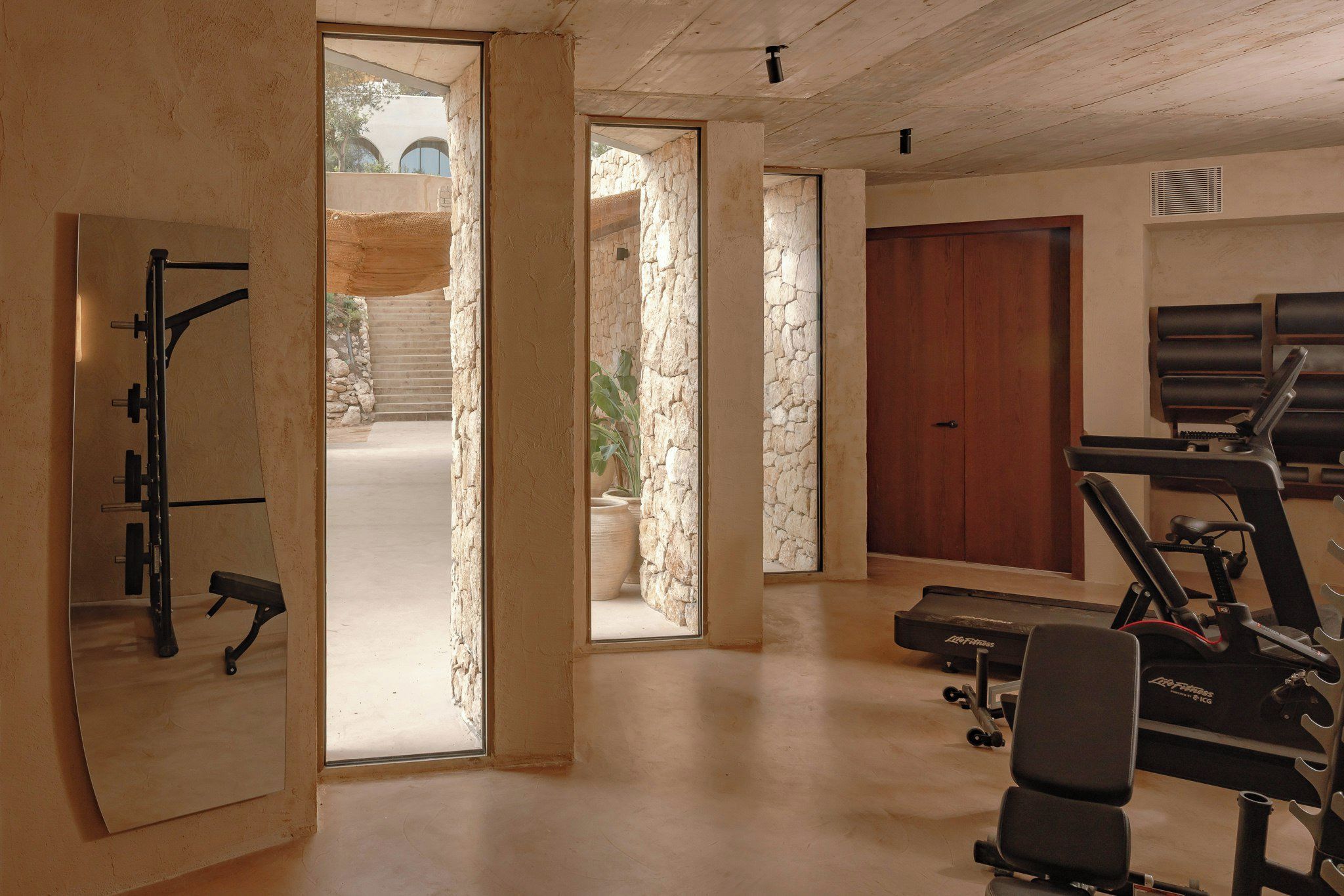 Un gimnasio con equipo de ejercicio, una banca y una puerta que da a un espacio exterior.