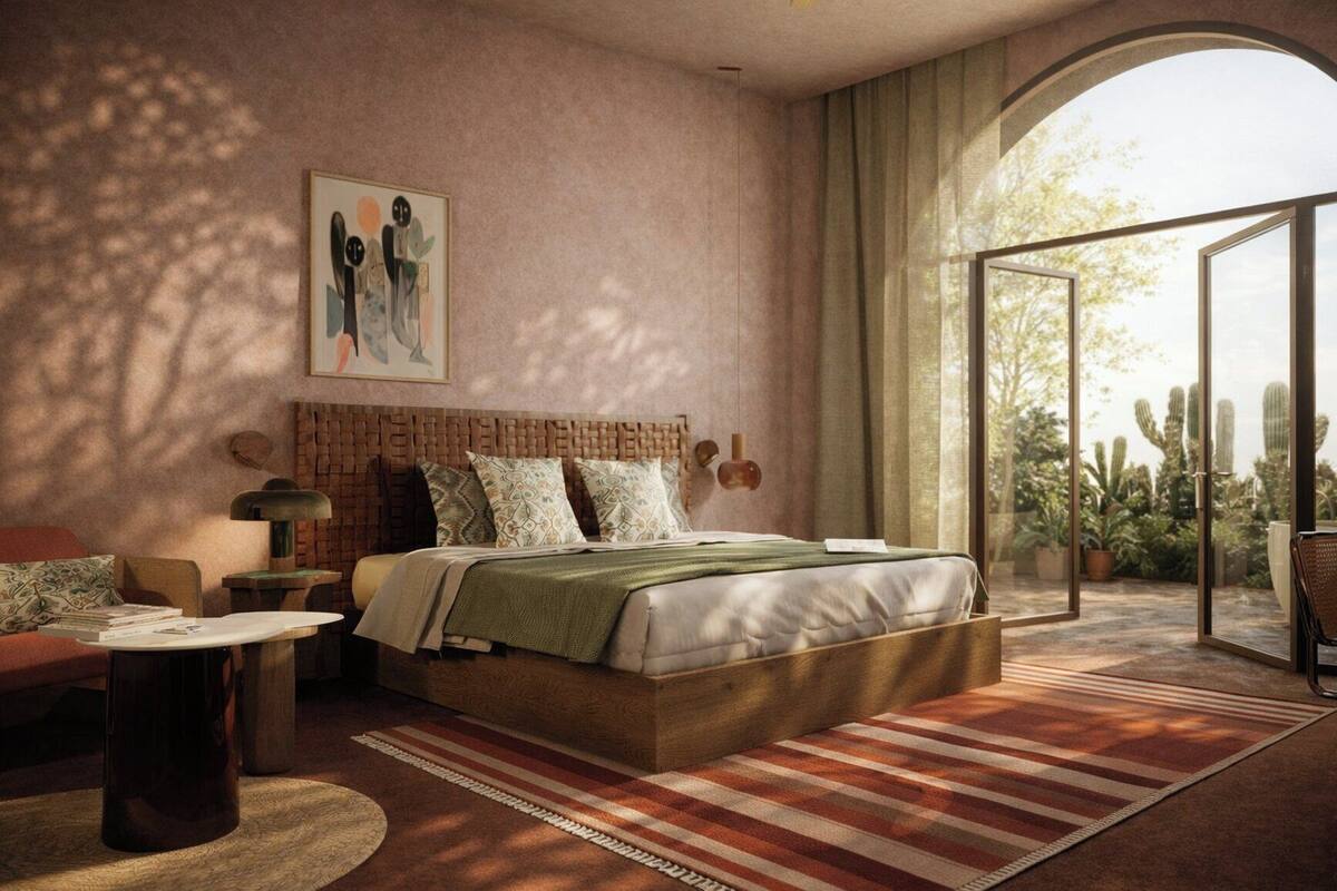 A bedroom with a bed, a nightstand, a chair, a window with a view of cacti, and a wall with a textured pattern.