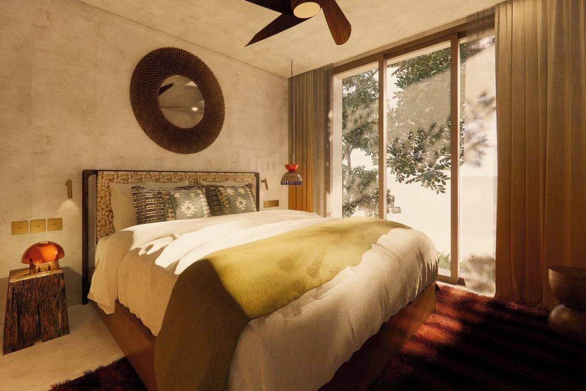 A bedroom with a bed, a round mirror, a ceiling fan, a nightstand, and a window with a view of trees.