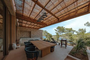 Un espacio de estar al aire libre techado con un fondo de pared de piedra, una mesa de madera y sillas de mimbre.