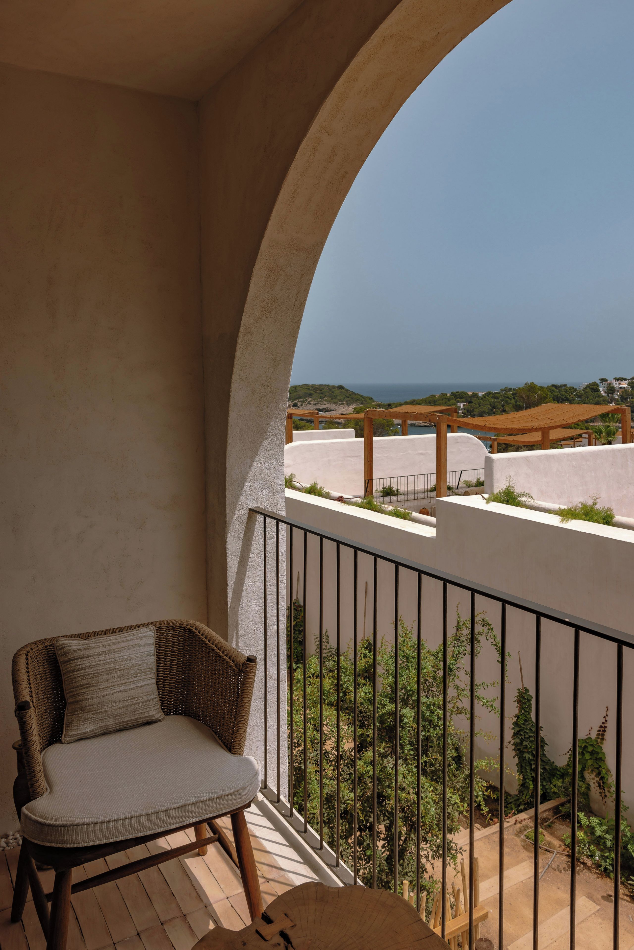 A balcony with a wicker chair, a view of the sea, and a clear sky.