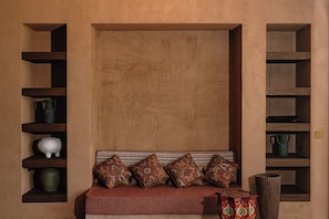Una habitación con un banco de madera, cojines estampados y estantes con adornos.