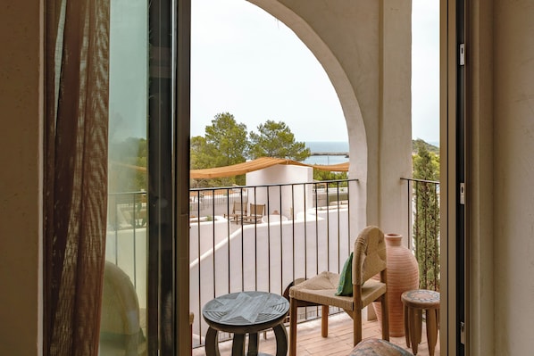 Un balcon avec vue sur la mer, une chaise, une petite table et une plante en pot.
