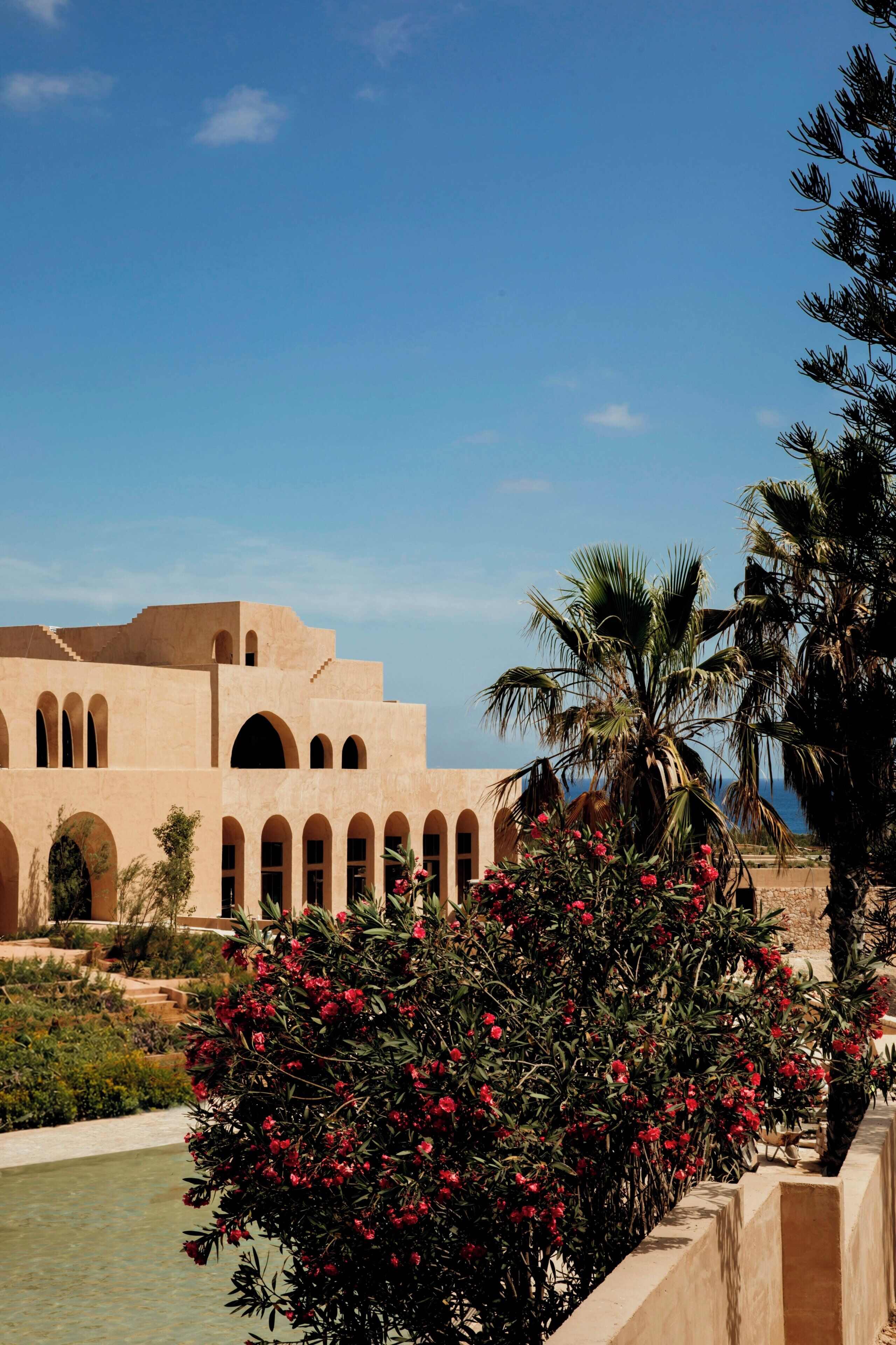 A building with multiple arches and a pool area with red flowers.