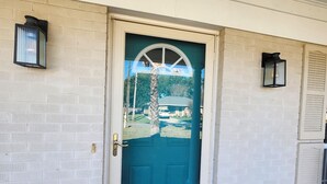 Uma porta azul-esverdeada com moldura branca, com dois candeeiros fixados na parede.