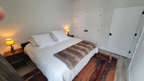 Un dormitorio con cama, dos lámparas de noche, una alfombra y armarios blancos.