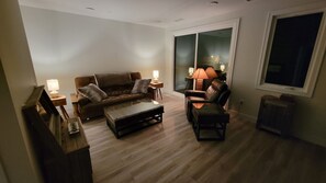Ett vardagsrum med en brun soffa, en fåtölj i läder, ett soffbord i trä och två lampor på sidoborden.
