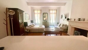 A bedroom with a bed, a desk, a chair, a sofa, a fireplace, and a window with curtains. - Le 100% Uzès, Right in the Historic Center (Uzès)