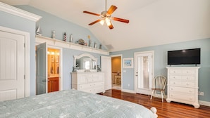 A bedroom with a bed, a ceiling fan, a dresser, a television, and a chair. - Walk to Beach! Sunny 5BR Oak Island Oasis (Oak Island)