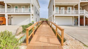 A wooden boardwalk leading to a residential building with multiple balconies and garage doors. - Walk to Beach! Sunny 5BR Oak Island Oasis (Oak Island)