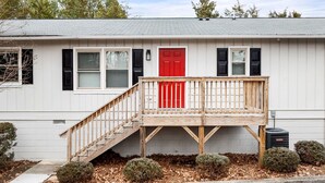 Une maison de plain-pied avec une porte rouge, un porche en bois et un petit escalier menant à l’entrée.
