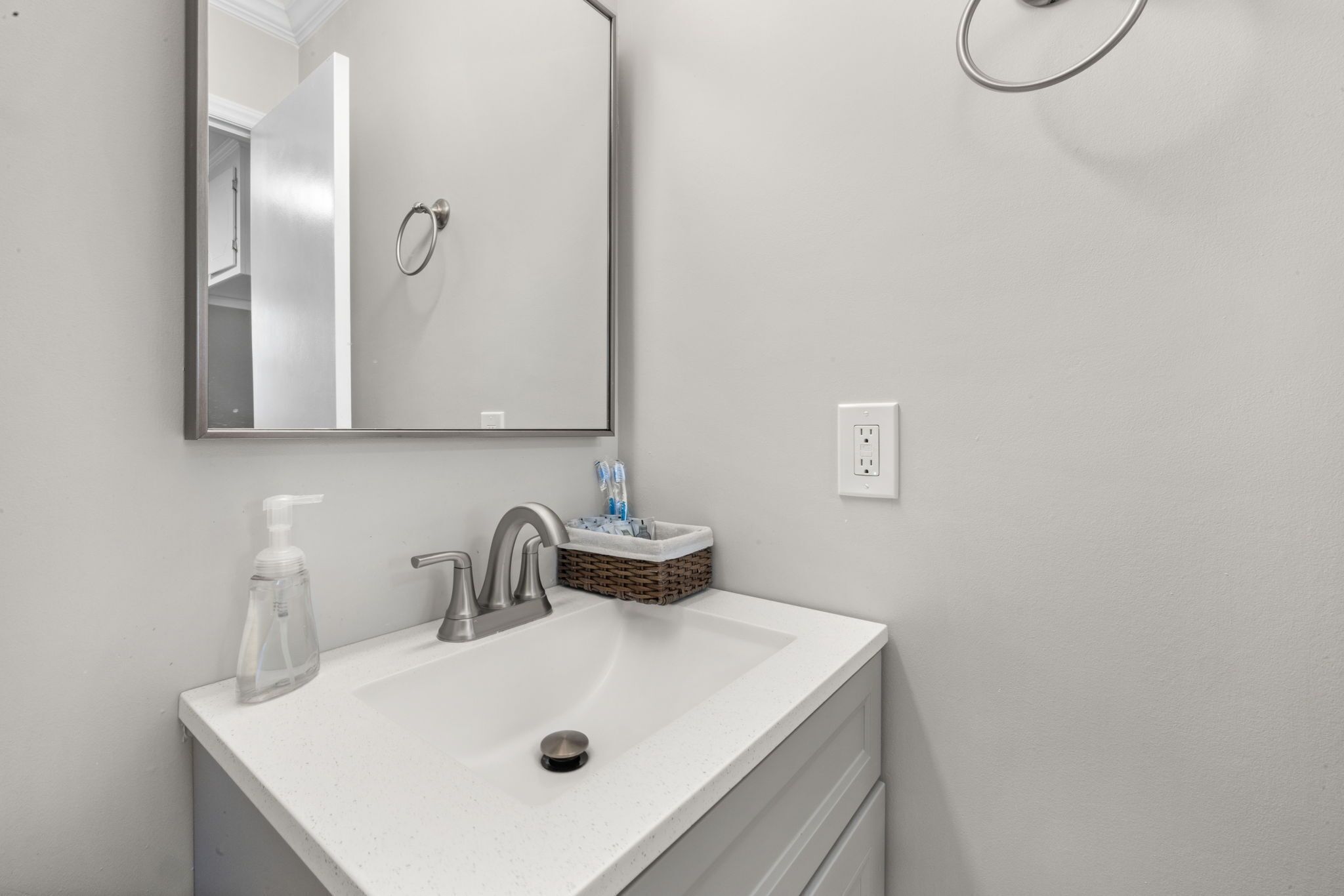 A bathroom with a white sink, a mirror, a soap dispenser, and a toothbrush holder.