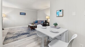 Un salon moderne avec un canapé blanc, une table basse et un coin repas comprenant une table et des chaises blanches.