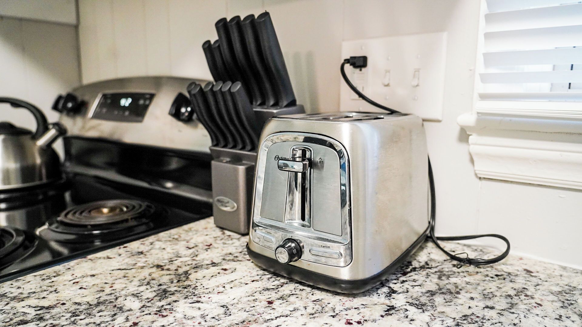 A kitchen with a stainless steel toaster, a stove, and a kettle.