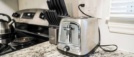 A kitchen with a stainless steel toaster, a stove, and a kettle.