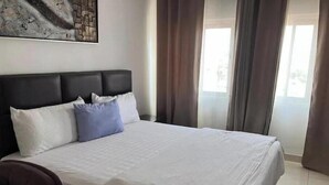 Un letto rifatto con cuscini bianchi e blu, una testata scura e un grande quadro astratto appeso alla parete.