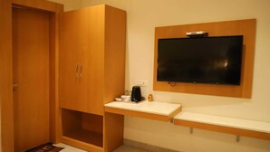 A hotel room with a wooden wardrobe, a small desk with a coffee maker, and a mounted TV. - Ananda Castle (Vrindavan)