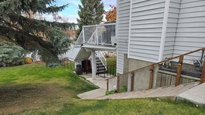 A residential property with a covered outdoor staircase leading to a deck, surrounded by a well-maintained lawn and trees.