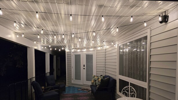 A covered patio area with string lights, a seating arrangement including a table and chairs, and a door leading to an interior space.