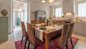 Un comedor con mesa de madera, sillas tejidas y un tapete rojo estampado.
