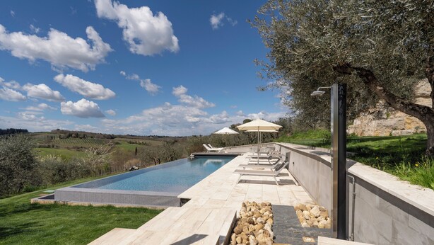 Una piscina con plataforma de piedra, sombrillas exteriores y vistas al campo.